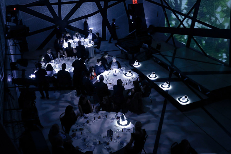 Seated dinner at round tables inside the hall under projected green imagery