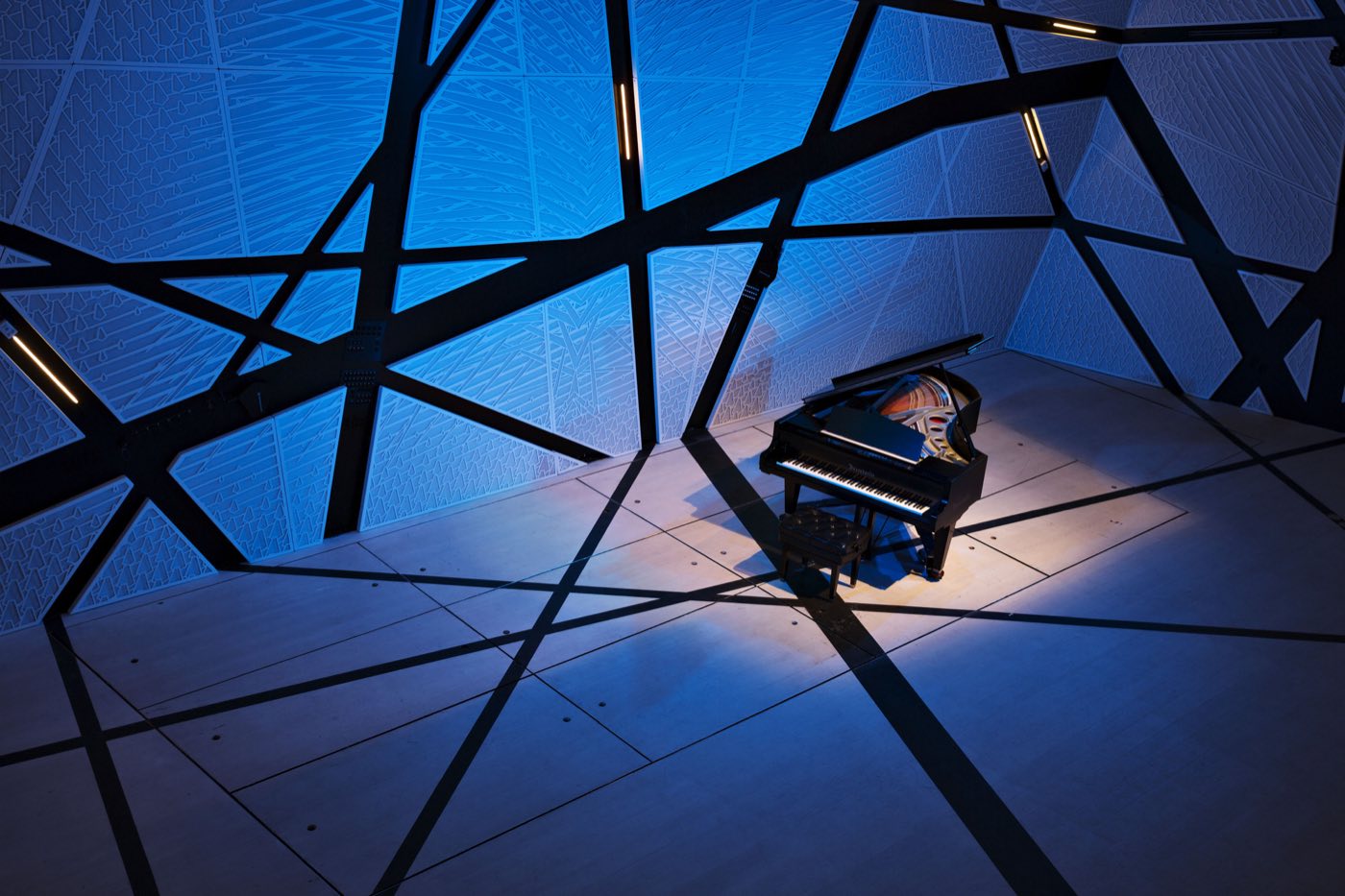 Hall washed in blue light with a single grand piano under angular beams