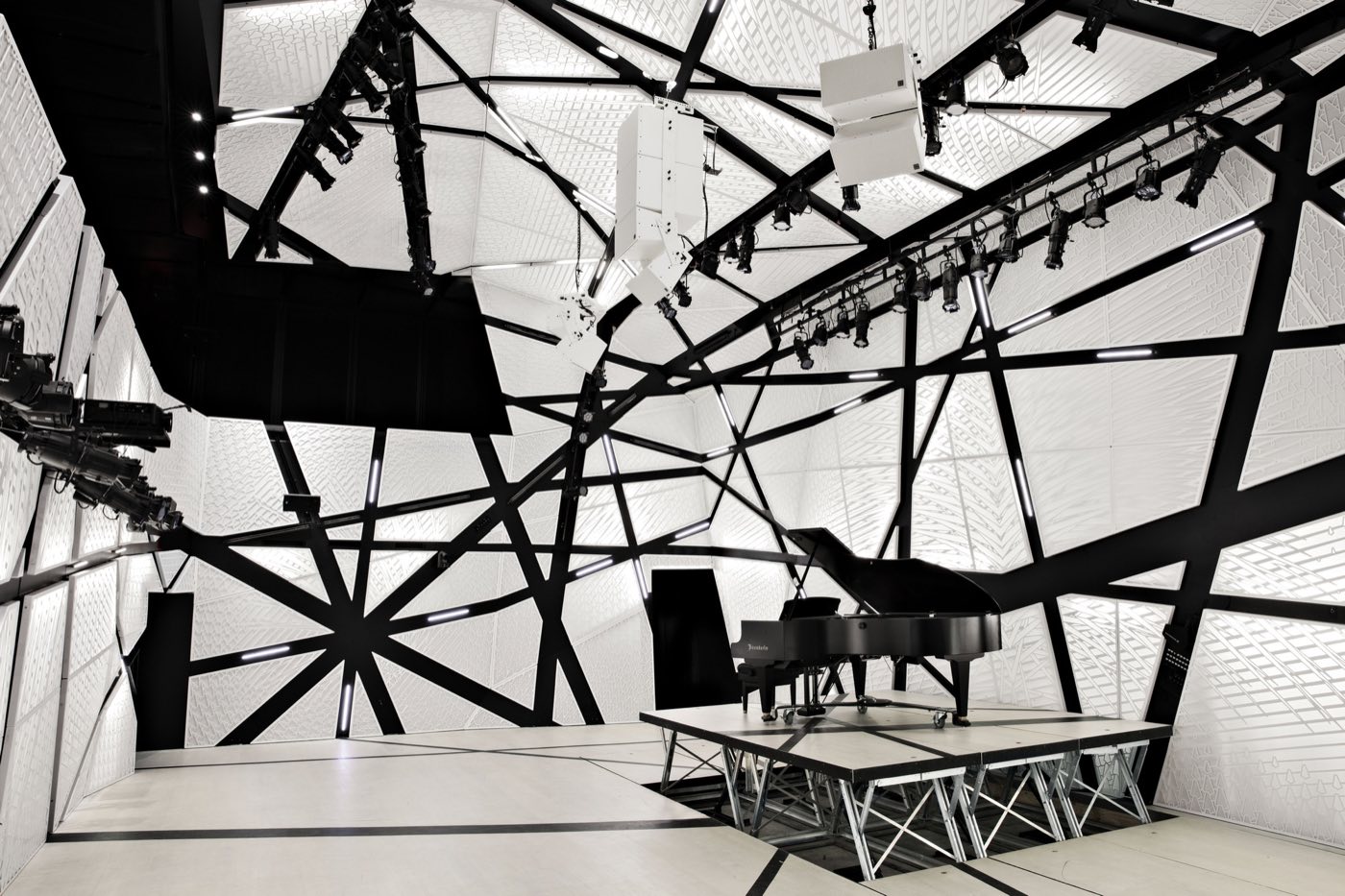 Raised stage with grand piano beneath a lighting grid and faceted white wall panels